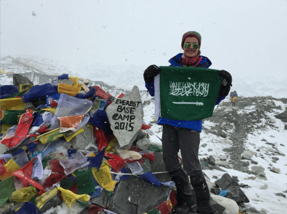 Dr Nasreen Alhokail holding a Saudi flag next to a colourful pile of bunting and a rock with the words Everest Base Camp 2015